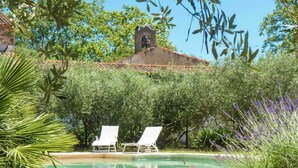 A pool area with two lounge chairs, surrounded by lush greenery and a bell tower in the background. - Holiday Home in Murviel with French Garden (Murviel-Les-Beziers)