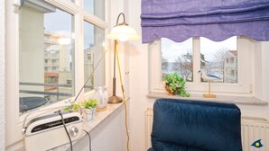 Una habitación con ventana, lámpara, silla y radiador.