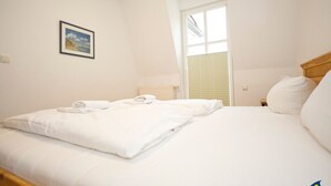 Una habitación de hotel con cama, ventana con persianas, un cuadro colgado en la pared y una mesita de noche.