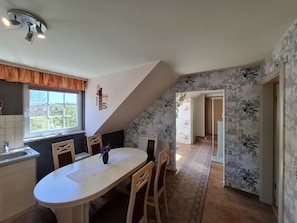 Un comedor con una mesa, sillas y un ventanal. Hay un ventilador de techo sobre la mesa.