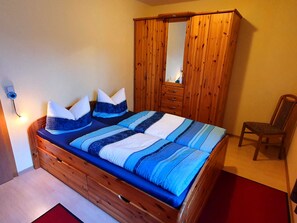 Un dormitorio con una cama de madera, un armario de madera, una silla y una mesita de noche.
