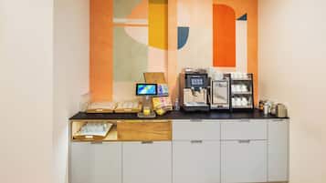 Eine Kaffeestation mit digitalem Bildschirm, Kaffeemaschine sowie verschiedenen Kaffeetassen und Behältern.