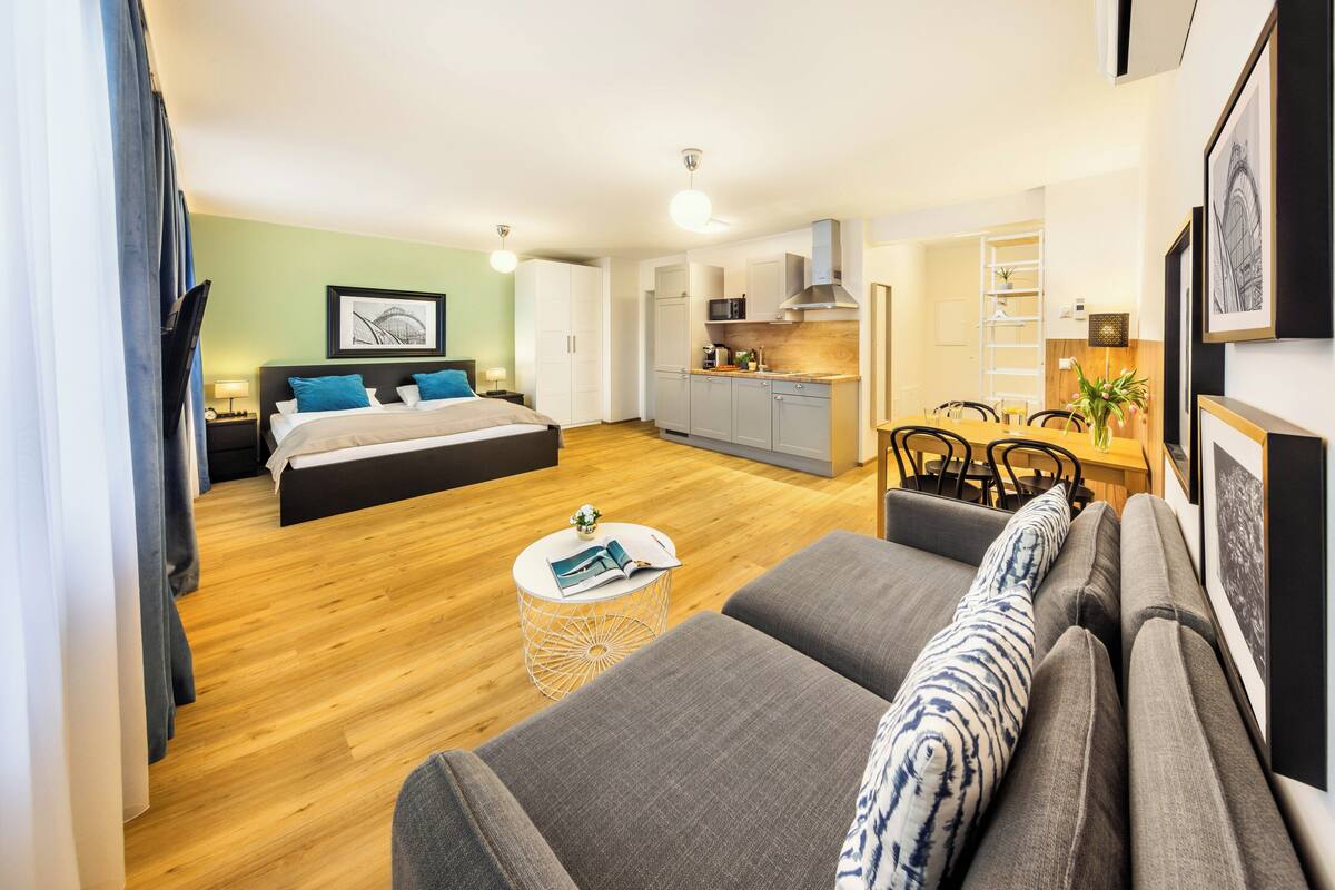 A modern hotel room with a bed, a sofa, a dining area, and a kitchen.