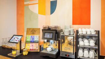 A coffee station with a digital ordering screen, a coffee machine, and a display of cups and mugs.