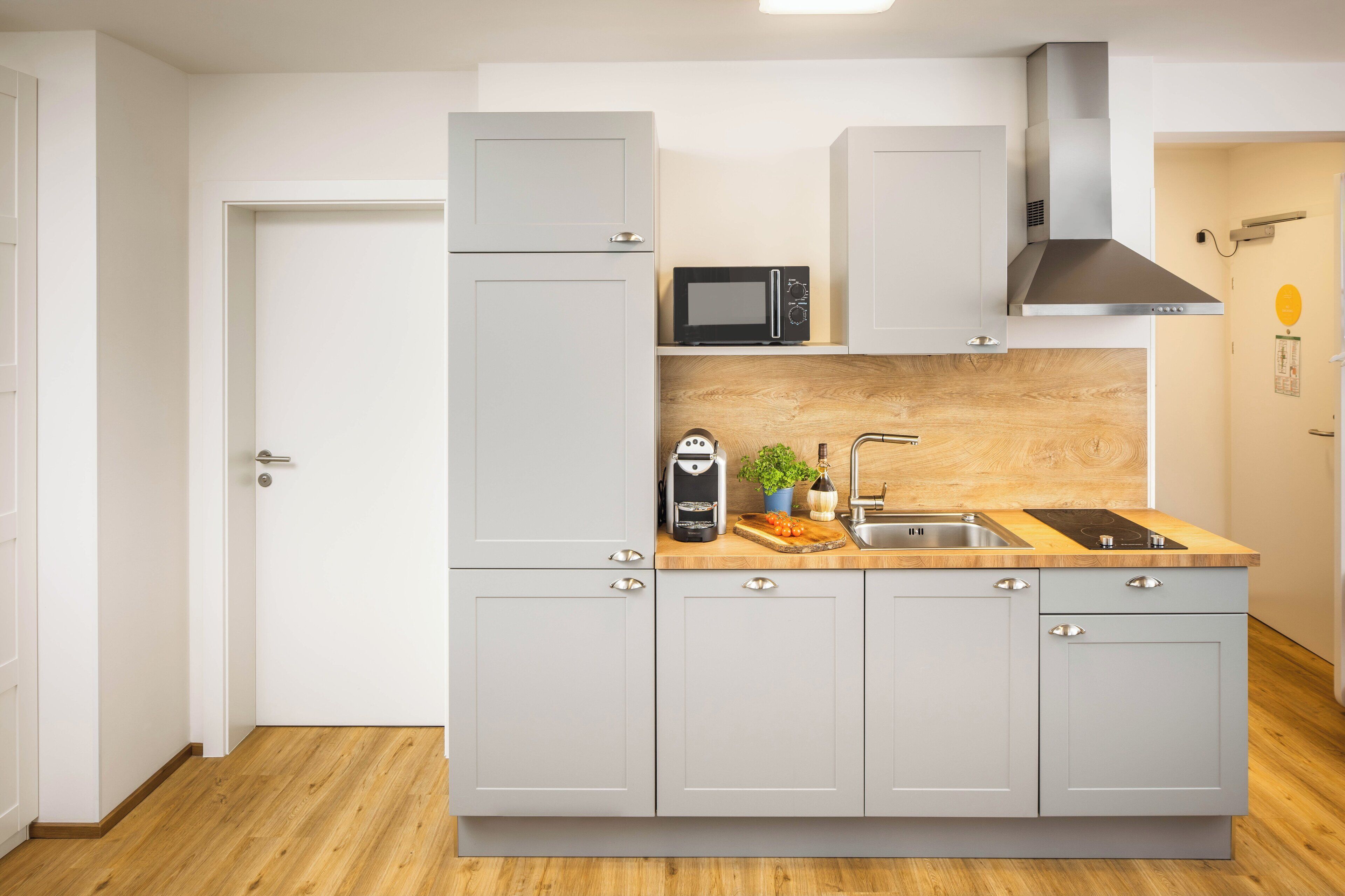 Cocina compacta con microondas, cafetera y lavamanos.