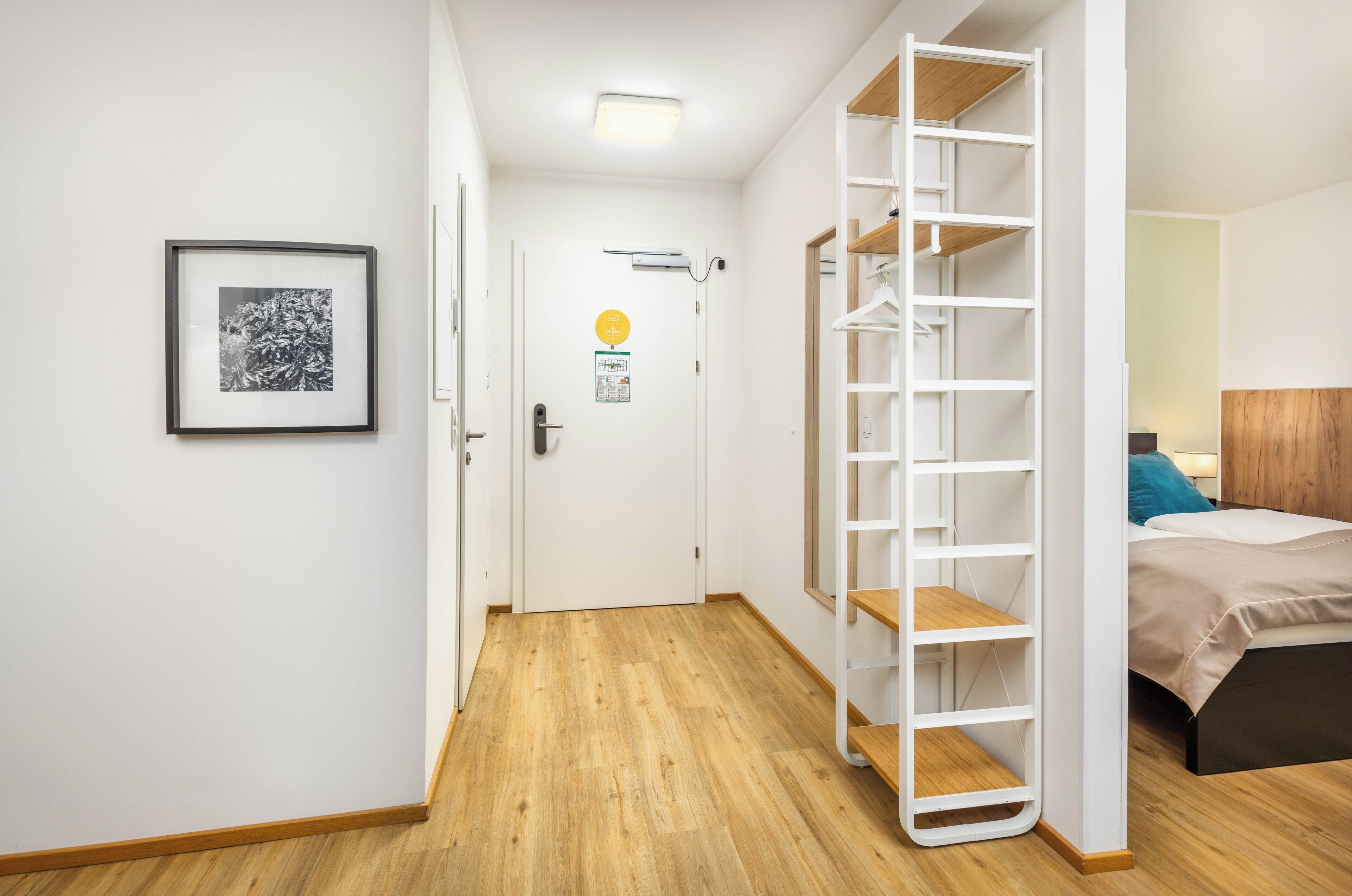 Un dormitorio con cama, un armario blanco, un cuadro enmarcado en la pared y una puerta con un cartel.