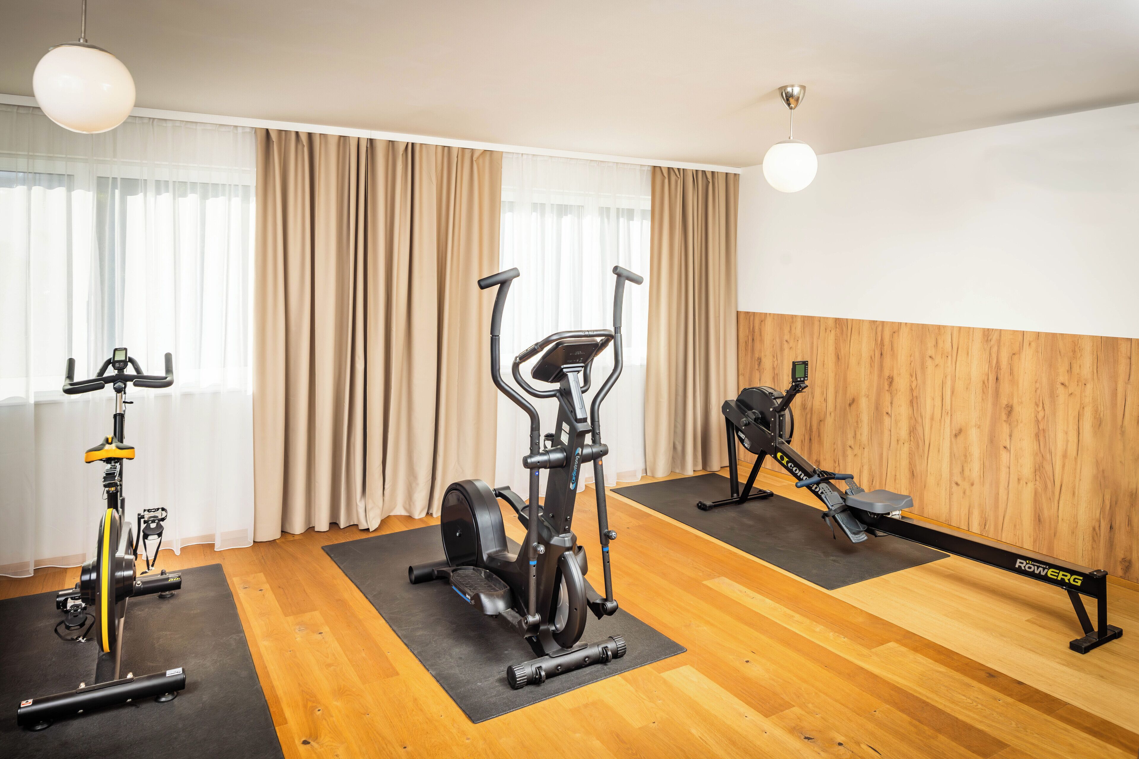 A fitness room with an elliptical, a stationary bike, and a rowing machine.