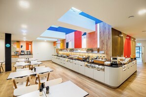 A modern cafe with a central counter, multiple seating areas, and a skylight. - Citadines South Vienna (Vienna)