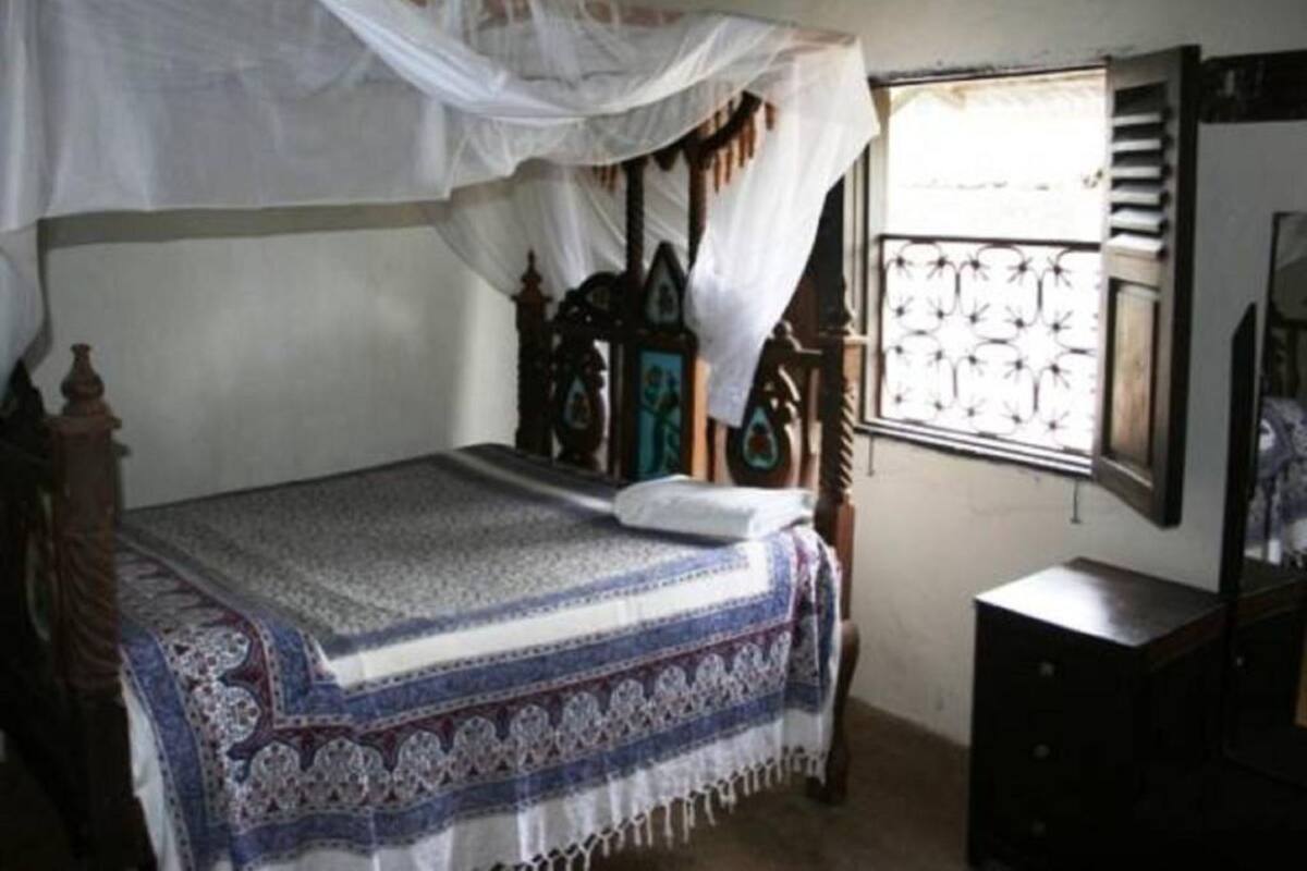A bedroom with a bed covered by a white canopy, a wooden headboard, and a patterned bedspread.