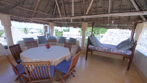 Un espacio de estar al aire libre con techo de paja, que incluye una mesa redonda con sillas, un sofá.