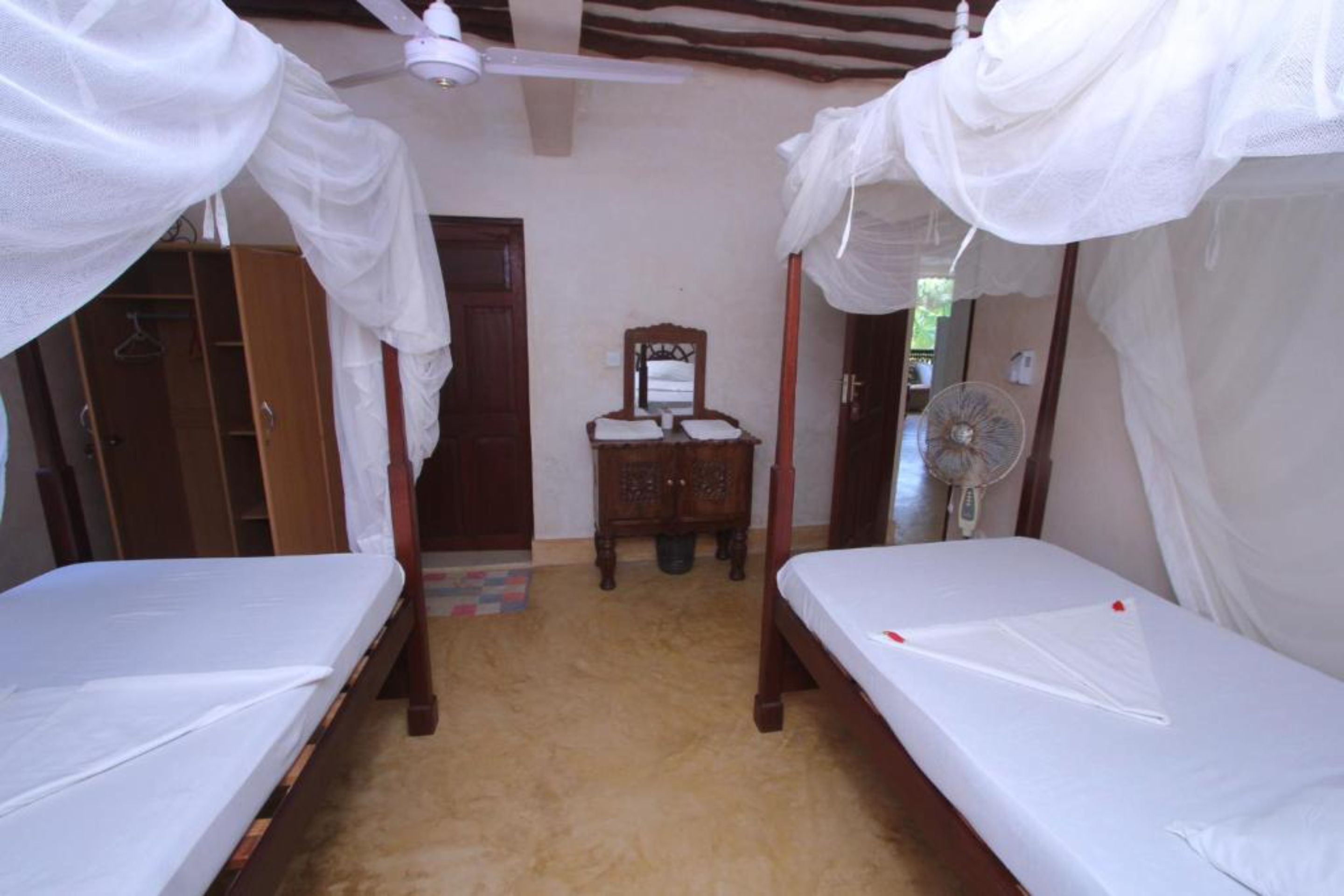 A room with two single beds, a wooden wardrobe, a mirror, and a ceiling fan.
