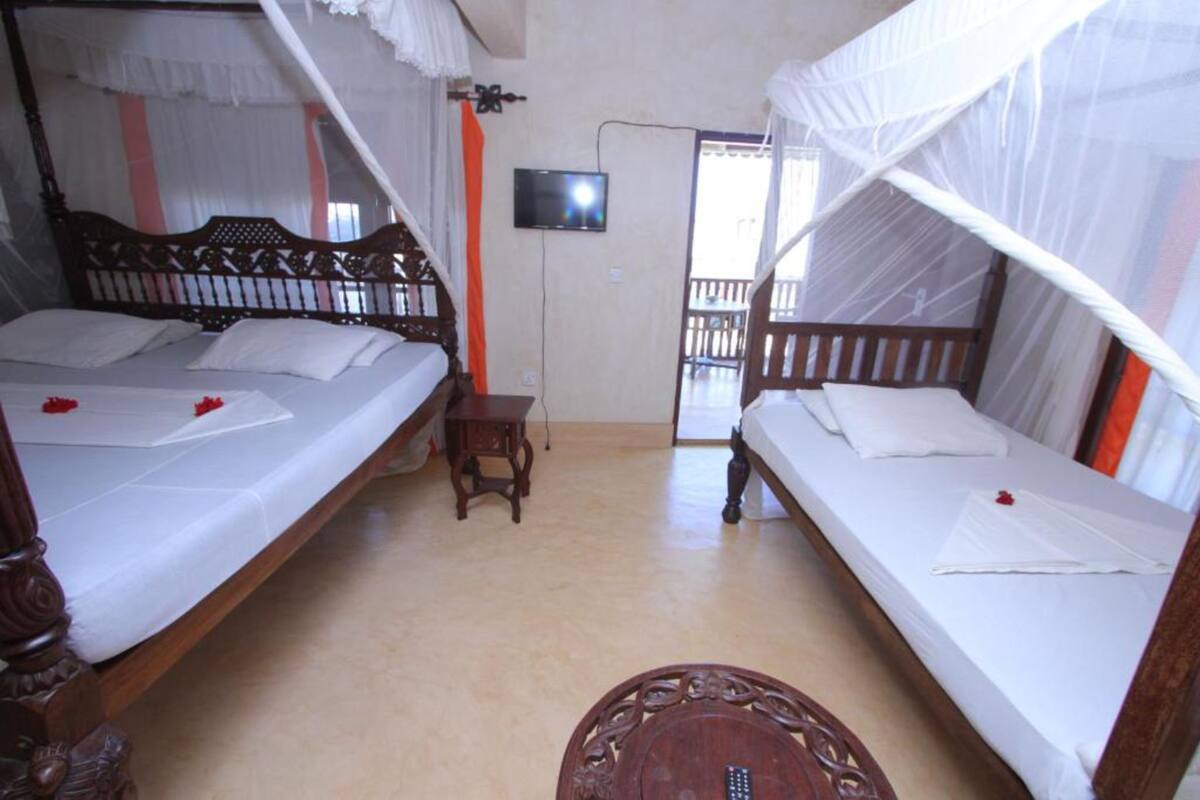 A room with two beds, each with a canopy, a television on the wall, and a small table.