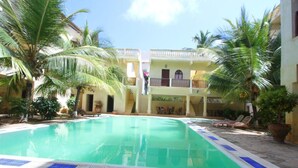 Una piscina con borde de azulejos, rodeada de palmeras y sillas de descanso.