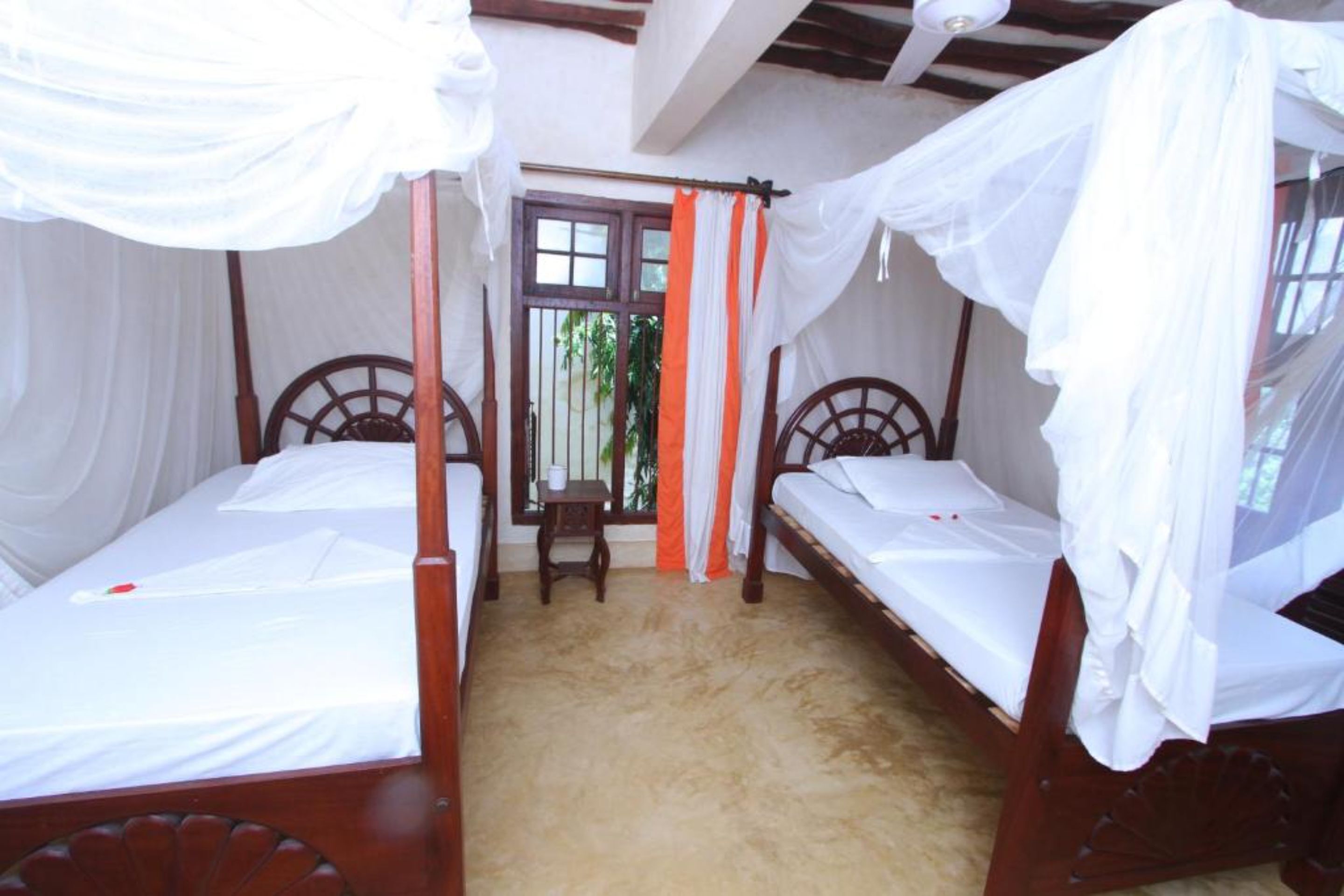 A room with two wooden beds, each with a canopy. There is a small table and a window with curtains.