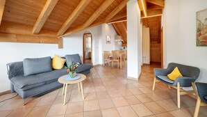 A spacious living area with a high wooden ceiling, a grey sofa, a small round table, and a dining area in the background. - Apartment 'Stettnerhof Penegal' with Mountain View, Terrace, Shared Garden & Wi-Fi (Völlan/Lana)