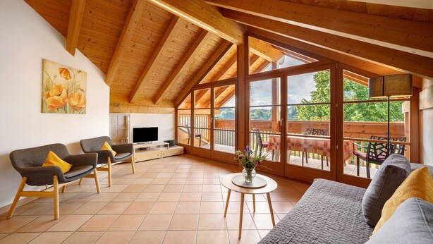 A spacious living area with wooden beams, large windows, a sofa, a TV, and a dining area. - Apartment 'Stettnerhof Penegal' with Mountain View, Terrace, Shared Garden & Wi-Fi (Völlan/Lana)