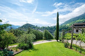A lush green landscape with a clear sky, a tall tree, and a building with a sloped roof.