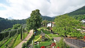 A vineyard with a playground, houses, and a mountain backdrop. - Apartment 'Stettnerhof Penegal' with Mountain View, Terrace, Shared Garden & Wi-Fi (Völlan/Lana)