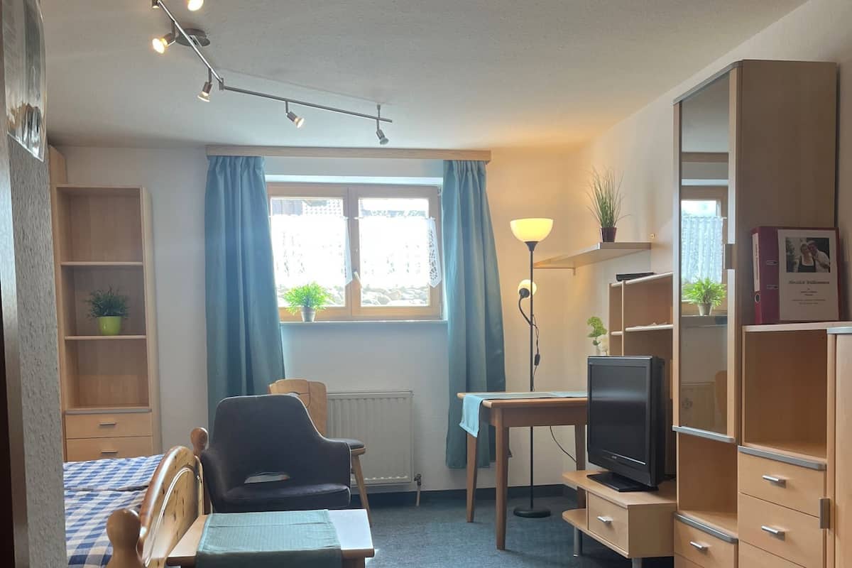 A compact room with a bed, a desk, a chair, a TV, and a bookshelf.