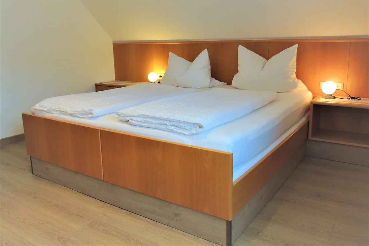 A double bed with a wooden headboard, two bedside tables with lamps, and a light-colored wooden floor.