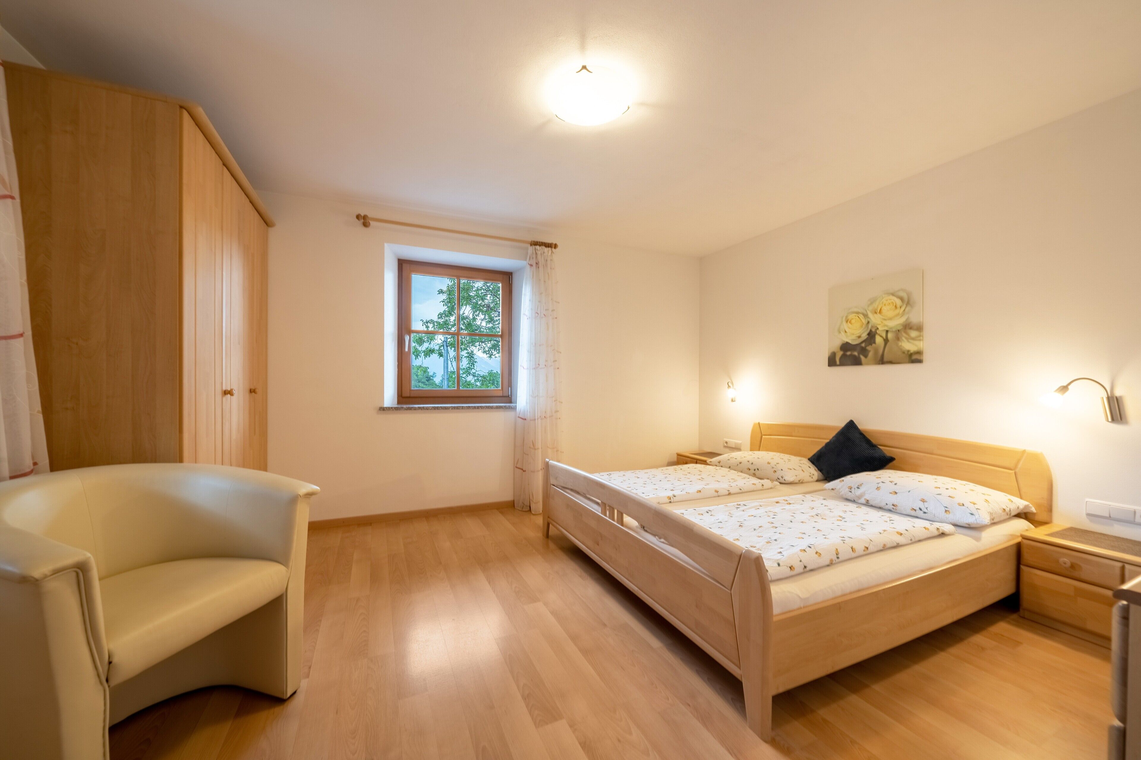 Een slaapkamer met een bed, een stoel, een raam en een schilderij aan de muur.