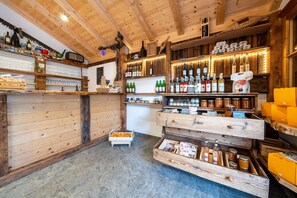 A rustic interior with wooden shelves displaying various bottles and jars, a counter with a cash register, and a tiled floor.