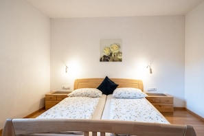 A double bed with floral bedding, two bedside tables, a nightstand, a wall-mounted light, and a framed picture above the bed.