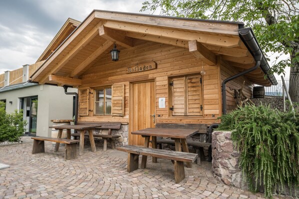 A wooden building with a sign reading 'Hofladen,' outdoor wooden benches, and a cobblestone ground.
