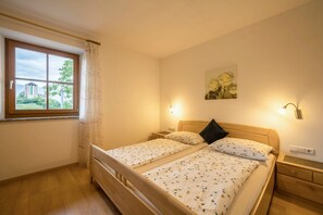 A bedroom with two beds, a window with curtains, a painting on the wall, and bedside lamps.