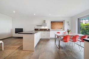 Une cuisine moderne dotée d’un îlot central, de meubles blancs et d’un coin repas avec des chaises rouges.