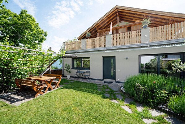 A modern house with a wooden deck, a stone pathway, and a well-maintained lawn.