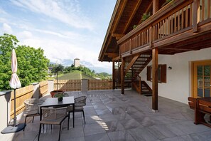 Um pátio com mesa e cadeiras, um deck de madeira e vista para uma colina com uma torre.