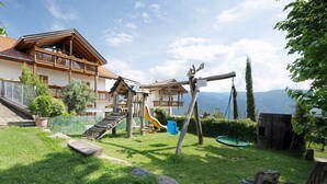 A chalet with a wooden deck, a slide, and a swing set in a grassy backyard. - Apartment 'Stettnerhof Mayenburg' with Mountain View, Terrace & Wi-Fi (Völlan/Lana)