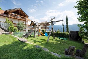 A chalet with a wooden deck, a slide, and a swing set in a grassy backyard.