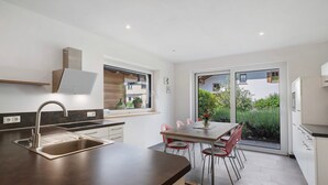 A modern kitchen with a large island, a dining area with chairs, and a sliding glass door leading to a garden. - Apartment 'Stettnerhof Mayenburg' with Mountain View, Terrace & Wi-Fi (Völlan/Lana)