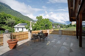 A patio with a table and chairs, surrounded by a wooden fence, overlooking a mountainous landscape.