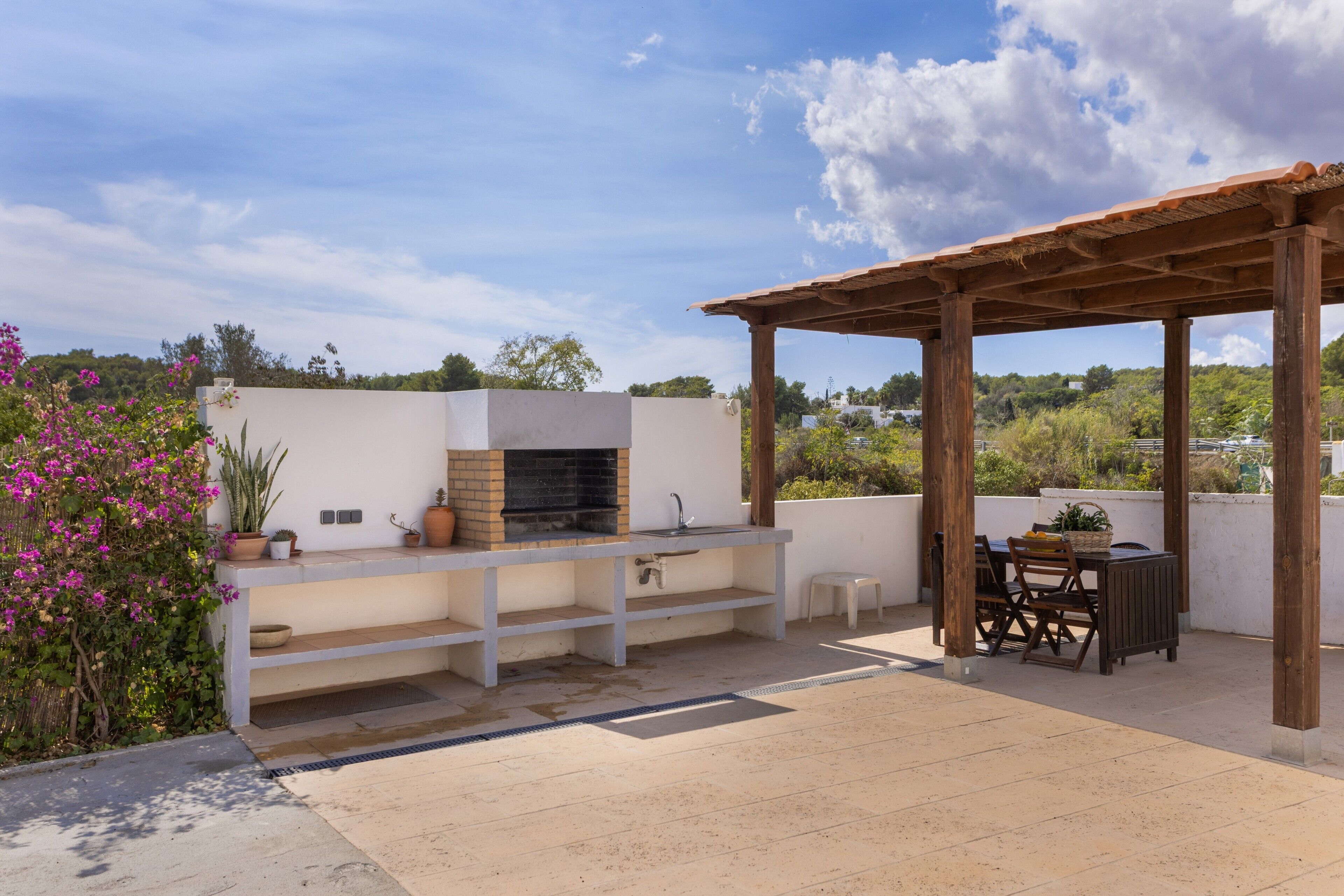 An outdoor patio with a barbecue grill, a sink, and a table with chairs.