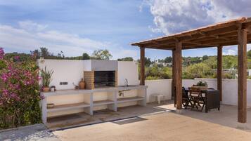 An outdoor patio with a barbecue grill, a sink, and a table with chairs.