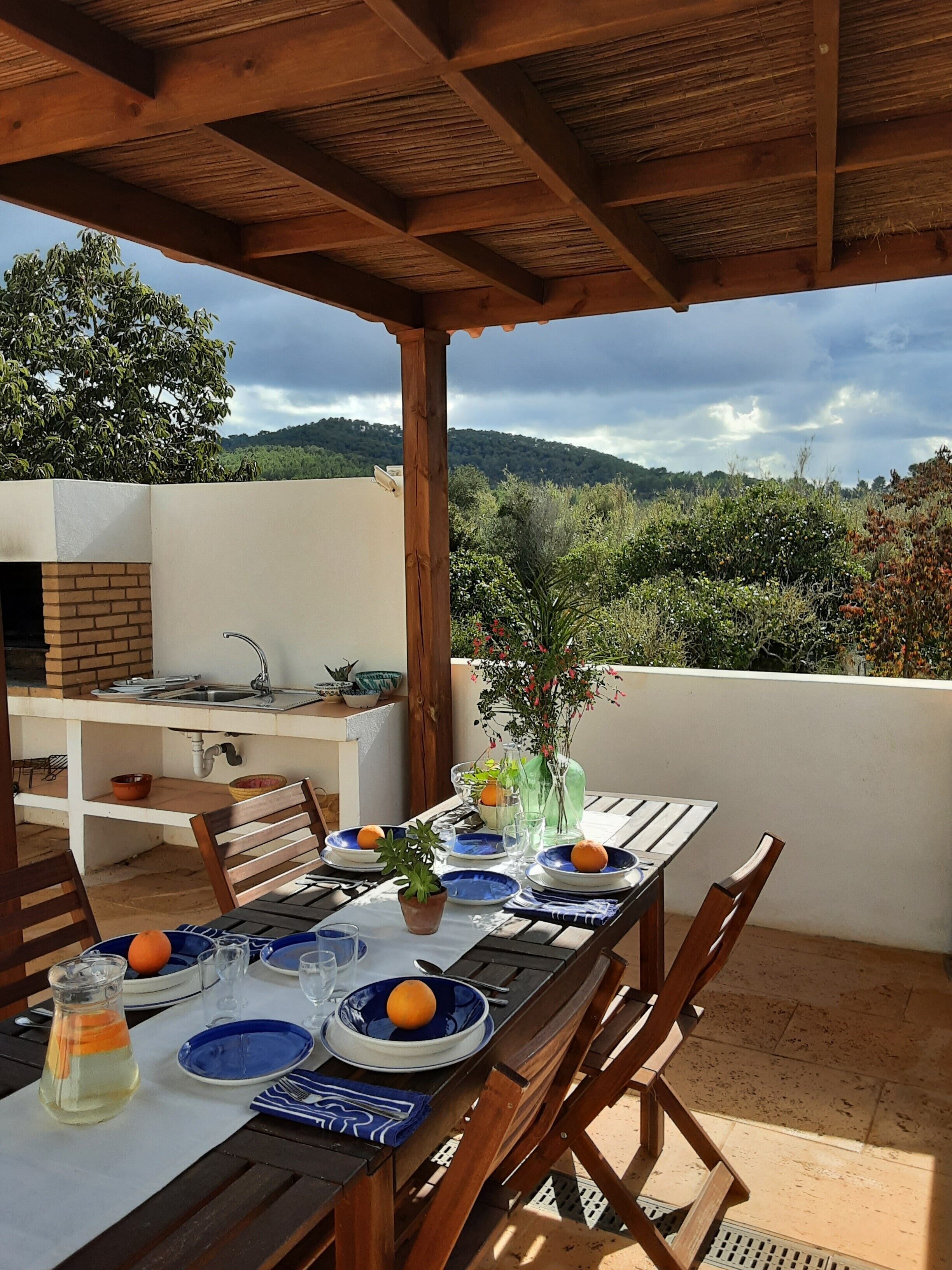 An outdoor dining area with a table set for two, a brick oven, and a view of the surrounding landscape.