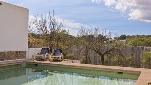 A swimming pool with two lounge chairs, a white wall, and a view of trees and a fence. - Country House That Welcomes Pets "Finca Can Paci" with Mountain Views (Santa Eulalia)