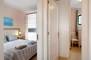 Une chambre à coucher avec un lit, une table de chevet, une lampe et une vue sur la salle de bain par une porte ouverte.