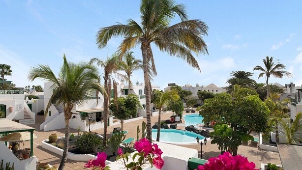 A pool area with palm trees, a clear sky, and white buildings. - Holiday Apartment 'Apartamento Rocas Negras' by the Beach with Pool View & Terraces (Puerto del carmen)
