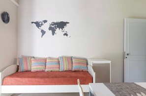 Ein Zimmer mit einem Bett, einer Wanddekoration mit Weltkarte, einem farbenfrohen Kissen-Set und einer weißen Tür.