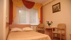 A bedroom with a bed, two chairs, a small table, and a window with curtains. - BELWEDER (Duszniki Zdroj)