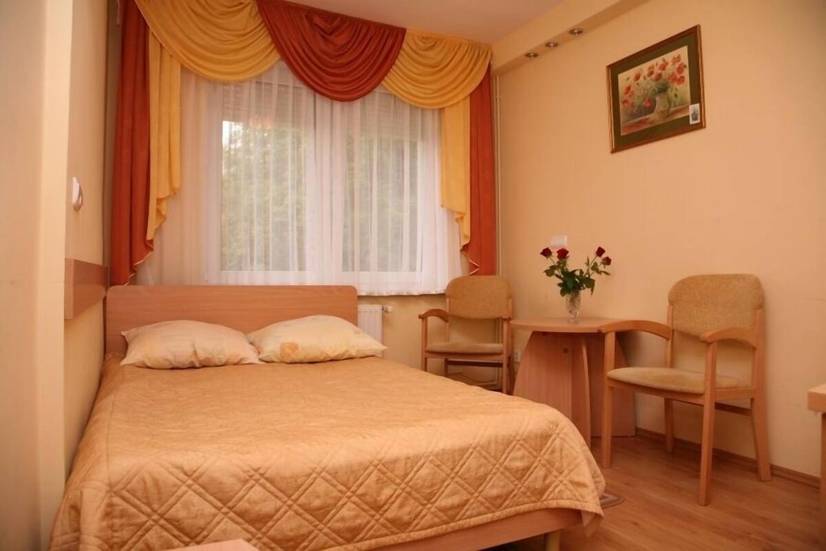 A bedroom with a bed, two chairs, a small table, and a window with curtains.