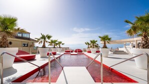 A pool area with red seating, palm trees, and a clear sky. - "Apartment Higueron Wave 1" with Sea View, Pool, Wi-Fi & Terrace (Fuengirola)