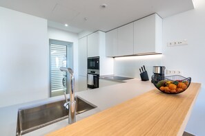 A modern kitchen with a stainless steel sink, a wooden countertop, a black fruit bowl, and a built-in oven.