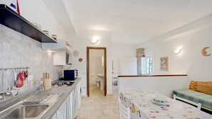 A compact kitchen with a sink, stove, and a dining area with a table and chairs. - Holiday Home "Casetta Antonella" with Mountain View, Garden & Terrace (Fraz. Lecchiore comune Dolcedo)