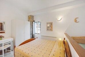 A bedroom with a bed, a desk, a chair, a radiator, a window, and a wall-mounted light fixture.
