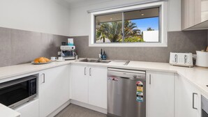 Una cocina moderna con lavavajillas incorporado, cafetera, tostadora y ventana con vista a palmeras.
